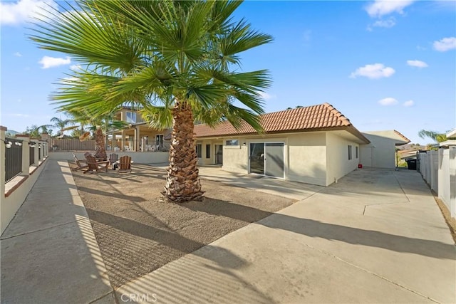 rear view of house with a patio area, a tiled roof, fence, and stucco siding