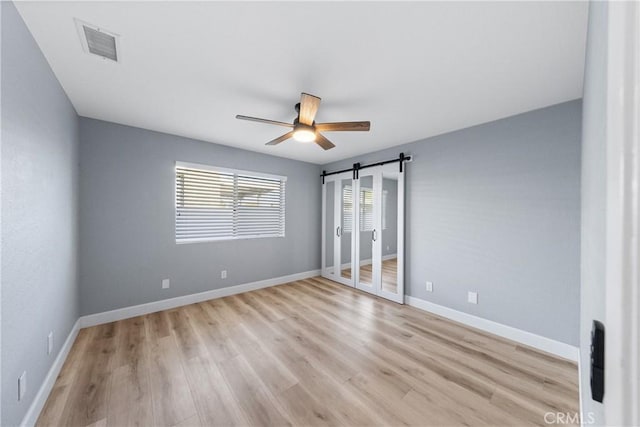 unfurnished bedroom featuring visible vents, a barn door, a ceiling fan, light wood-type flooring, and baseboards