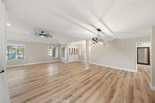 unfurnished living room featuring ceiling fan with notable chandelier, light wood-style flooring, and baseboards