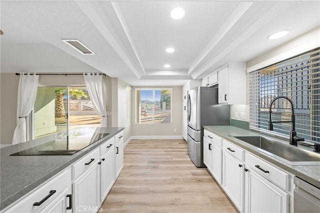 kitchen with a raised ceiling, visible vents, light wood-style flooring, appliances with stainless steel finishes, and a sink