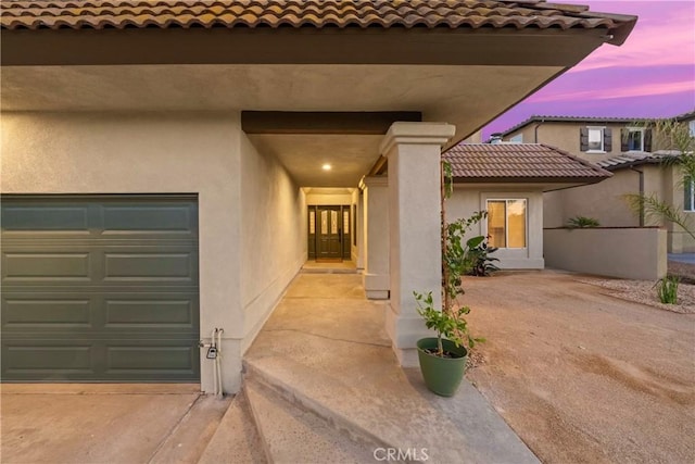 exterior entry at dusk with an attached garage and stucco siding