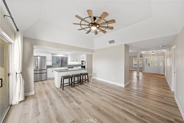 kitchen featuring open floor plan, white cabinets, a kitchen island, stainless steel fridge, and a kitchen bar