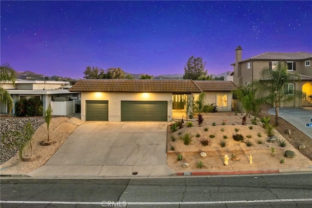 view of front facade with a garage, a tiled roof, concrete driveway, and stucco siding