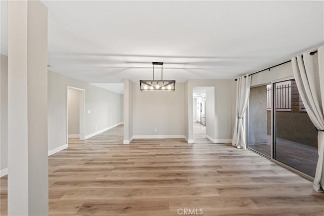 unfurnished dining area featuring light wood-style floors, washer / clothes dryer, a notable chandelier, and baseboards