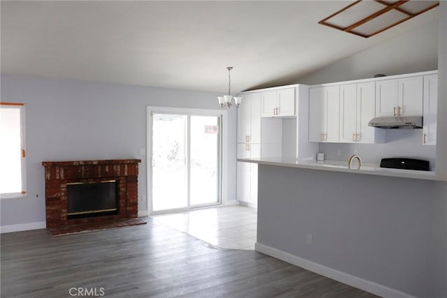 kitchen featuring vaulted ceiling, a brick fireplace, pendant lighting, wood-type flooring, and white cabinetry