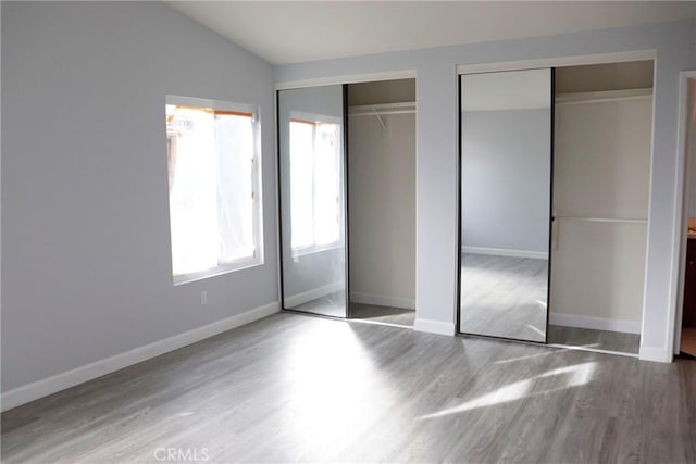 unfurnished bedroom with wood-type flooring, lofted ceiling, and multiple closets