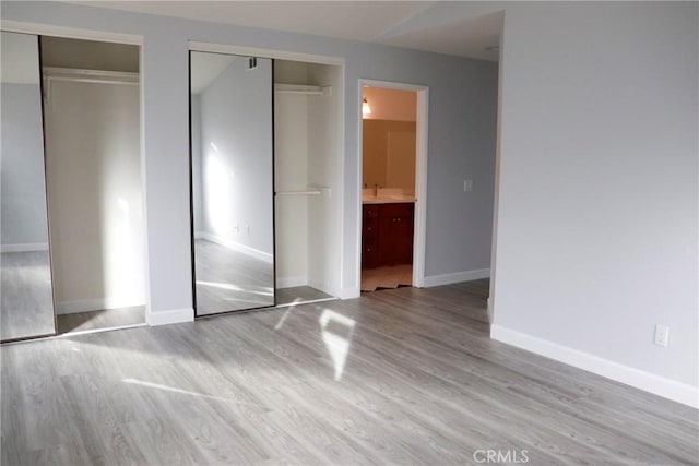 unfurnished bedroom with ensuite bathroom, light wood-type flooring, sink, and two closets