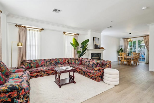 living room with a high end fireplace, crown molding, and light wood-type flooring