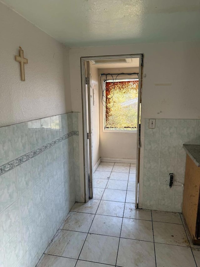 hall featuring tile walls, light tile patterned floors, and a textured ceiling