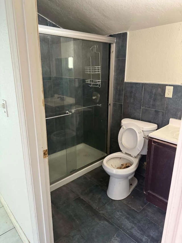 bathroom featuring a textured ceiling, vanity, tile walls, toilet, and walk in shower