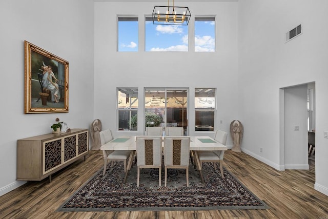 dining space featuring a chandelier, a healthy amount of sunlight, a towering ceiling, and wood-type flooring