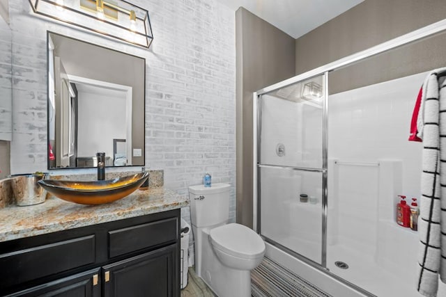 bathroom featuring a shower with door, brick wall, toilet, and vanity