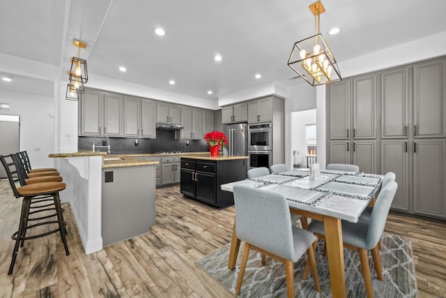 kitchen with gray cabinets, decorative backsplash, hanging light fixtures, a kitchen island with sink, and appliances with stainless steel finishes