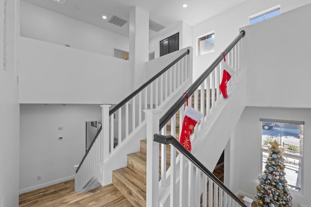 stairs featuring hardwood / wood-style flooring, plenty of natural light, and a towering ceiling