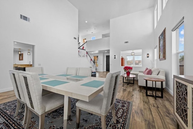 dining space with a wealth of natural light, a towering ceiling, and hardwood / wood-style floors