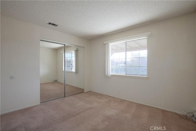 unfurnished bedroom with light carpet, a closet, and a textured ceiling