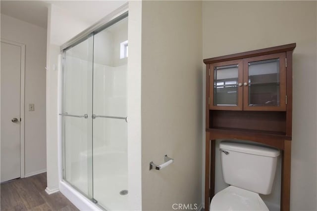 bathroom with toilet, a shower with shower door, and hardwood / wood-style floors