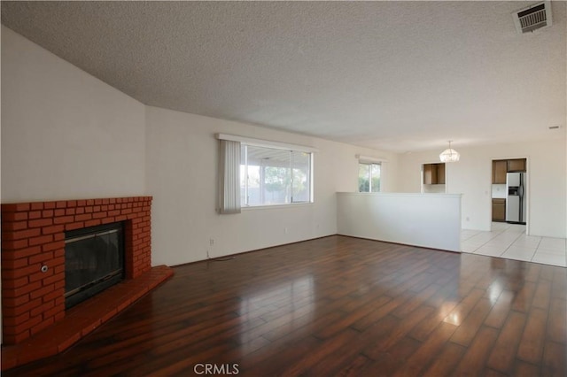 unfurnished living room featuring a brick fireplace, light hardwood / wood-style floors, and a textured ceiling