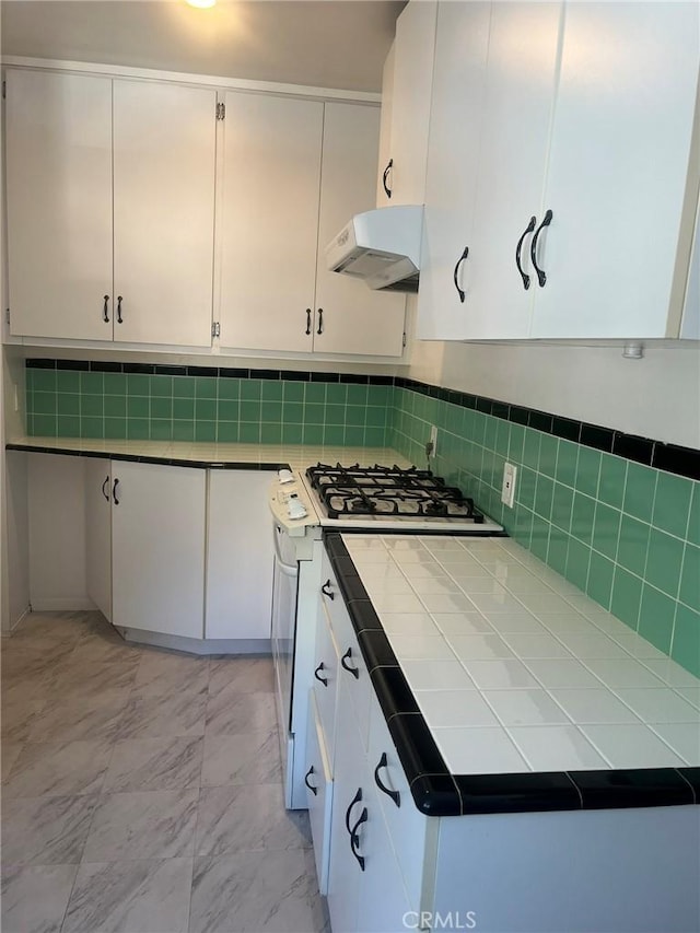 kitchen with white cabinetry, tile counters, decorative backsplash, white gas stove, and range hood