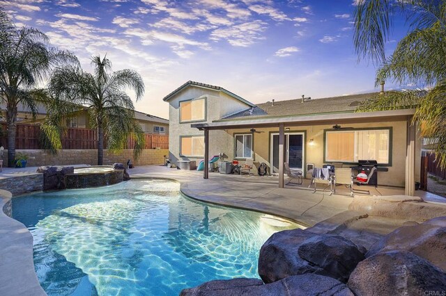 pool at dusk with ceiling fan, a patio area, and an in ground hot tub