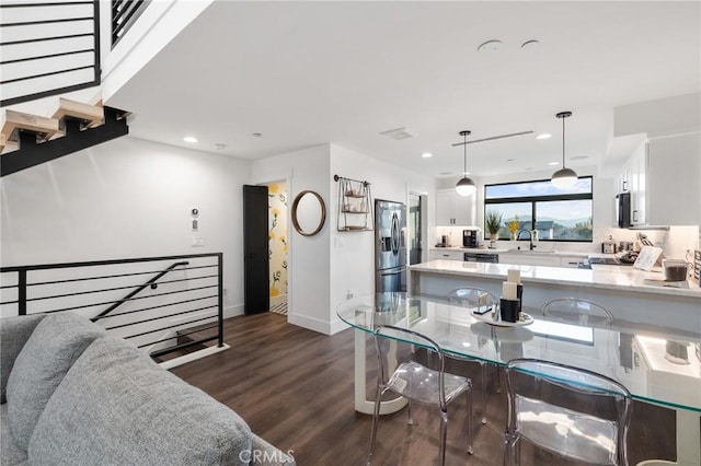 kitchen with pendant lighting, white cabinets, dark wood-type flooring, sink, and stainless steel fridge with ice dispenser