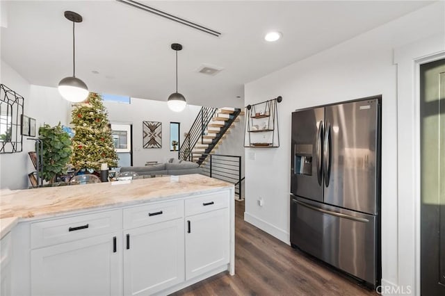 kitchen with light stone counters, white cabinetry, stainless steel fridge, and hanging light fixtures