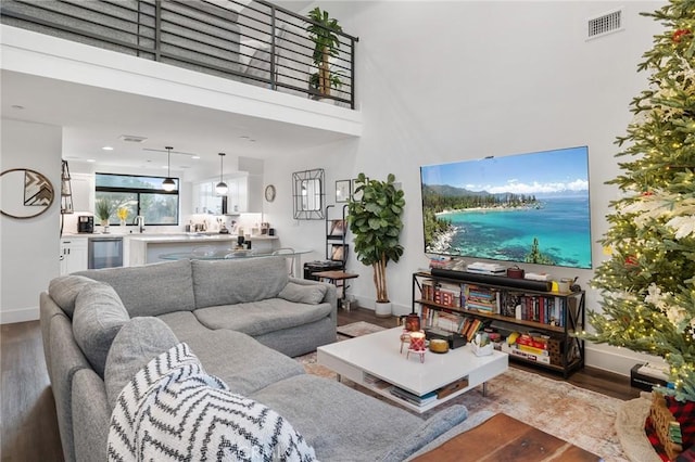 living room featuring sink, light wood-type flooring, a towering ceiling, and beverage cooler