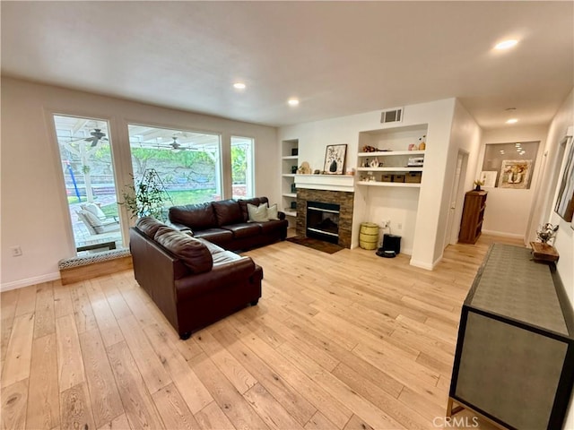 living room featuring ceiling fan, light hardwood / wood-style flooring, built in features, and a fireplace