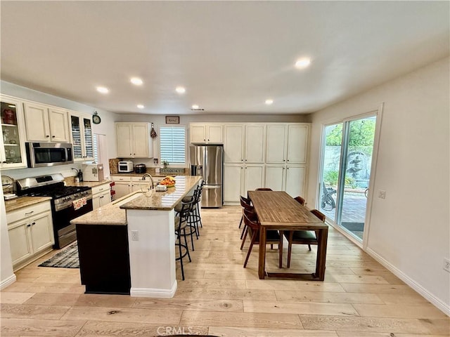 kitchen featuring light stone countertops, stainless steel appliances, sink, a kitchen island with sink, and a breakfast bar