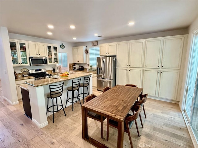 kitchen featuring stainless steel appliances, light wood-type flooring, dark stone countertops, a breakfast bar, and a center island