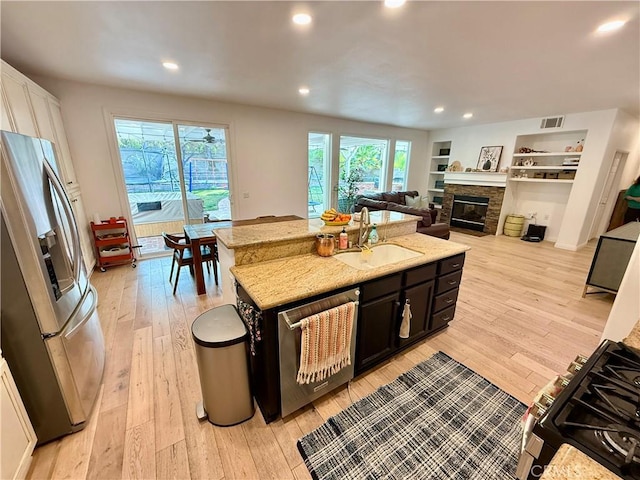 kitchen with appliances with stainless steel finishes, sink, light stone counters, and light hardwood / wood-style flooring