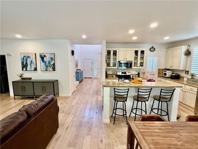 kitchen with an island with sink, a breakfast bar area, stainless steel appliances, light stone countertops, and light hardwood / wood-style flooring