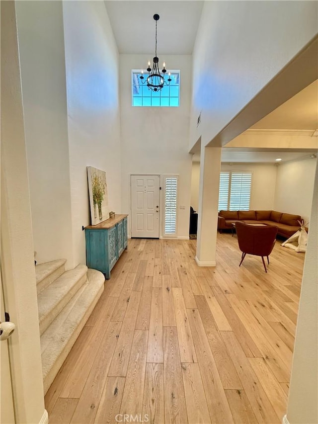 entrance foyer featuring light wood-type flooring, a towering ceiling, and an inviting chandelier