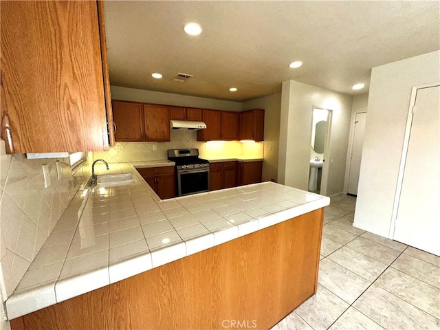 kitchen with kitchen peninsula, stainless steel stove, sink, and tile counters