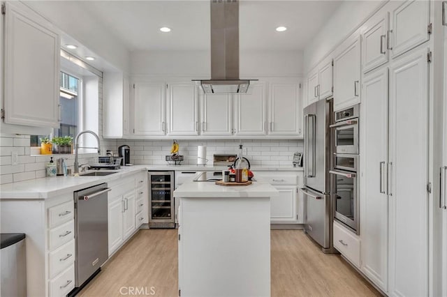 kitchen with white cabinets, beverage cooler, appliances with stainless steel finishes, a kitchen island, and island range hood