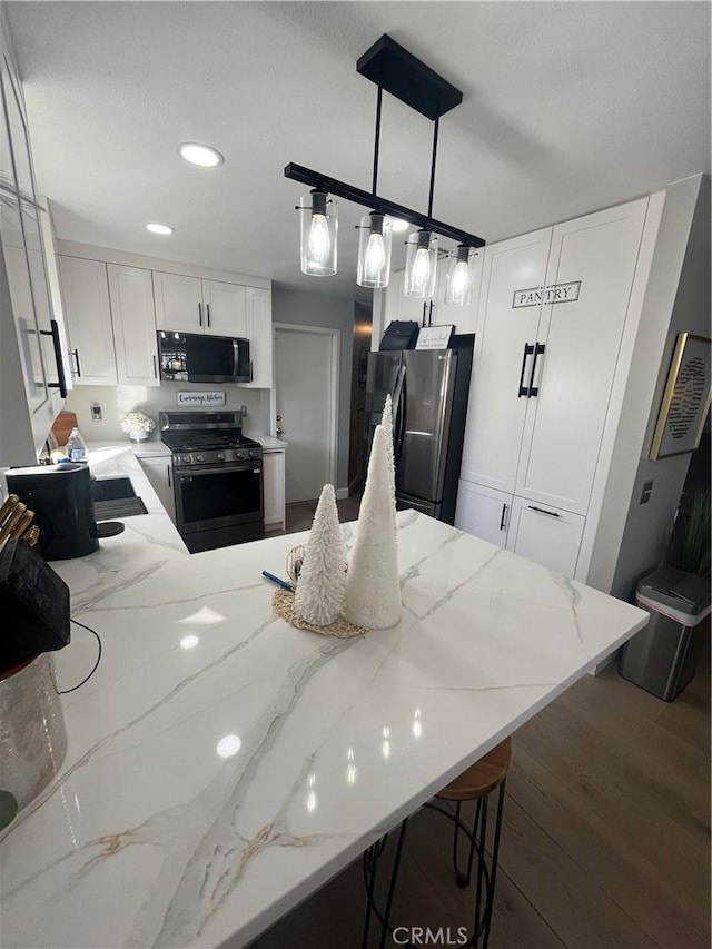 kitchen featuring white cabinets, light stone counters, stainless steel appliances, and pendant lighting