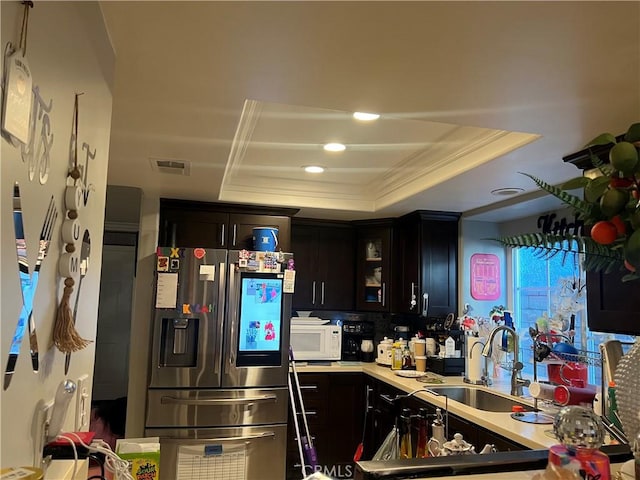 kitchen featuring stainless steel refrigerator with ice dispenser, a raised ceiling, dark brown cabinets, ornamental molding, and sink