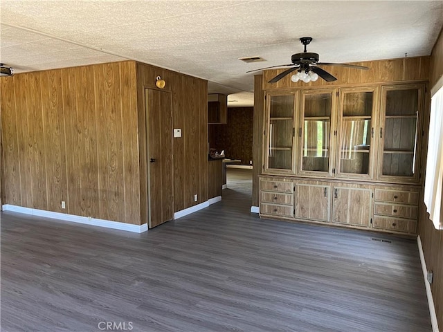 spare room featuring ceiling fan, dark wood-type flooring, and wooden walls