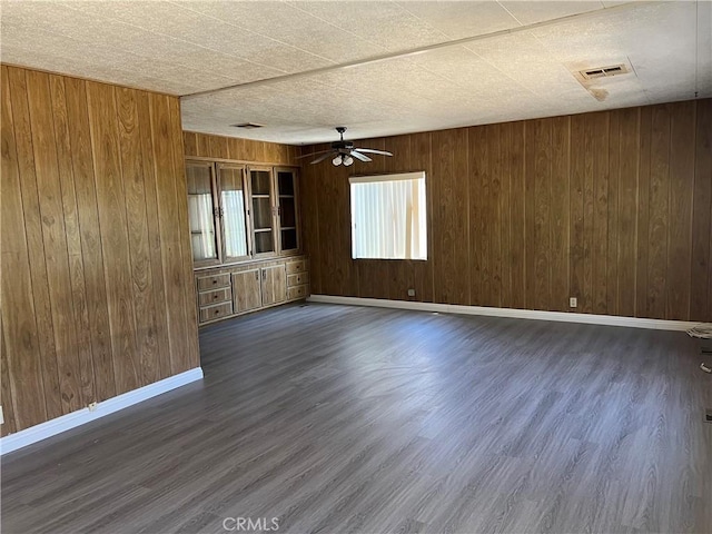 empty room featuring ceiling fan, dark wood-type flooring, and wooden walls