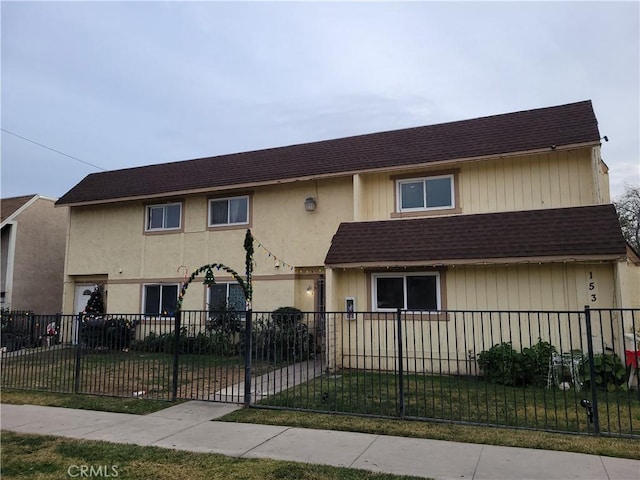 townhome / multi-family property featuring a fenced front yard, a shingled roof, and a front lawn