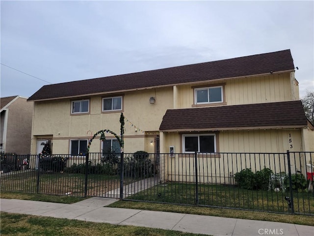 multi unit property featuring a fenced front yard, a front lawn, and a shingled roof