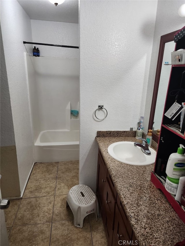 bathroom featuring a textured wall, bathing tub / shower combination, baseboards, vanity, and tile patterned floors