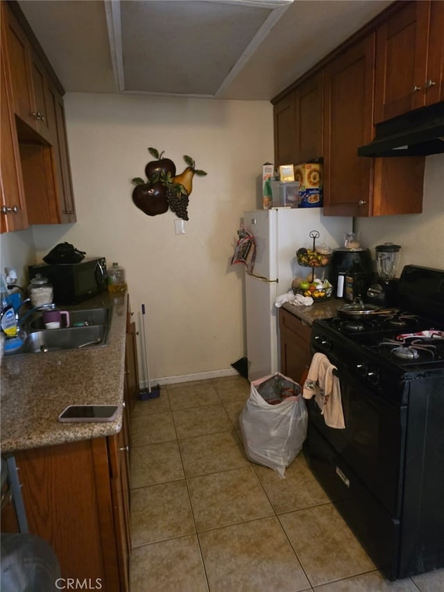 kitchen featuring light tile patterned floors, gas stove, a sink, under cabinet range hood, and baseboards