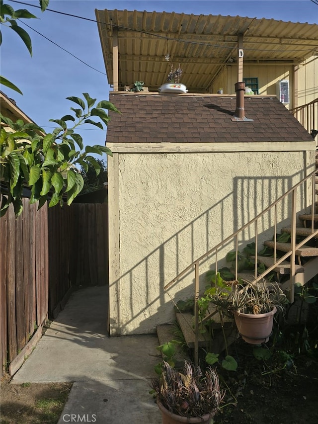 view of property exterior featuring a shingled roof, fence, and stucco siding