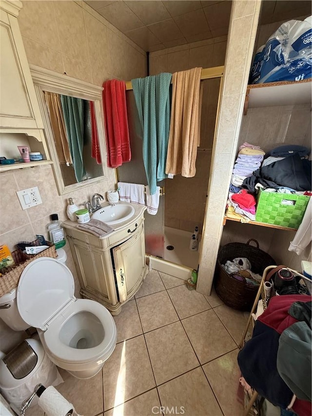 bathroom featuring toilet, vanity, tile patterned flooring, tile walls, and a shower with door