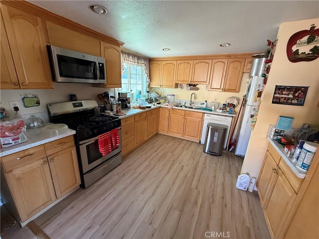 kitchen with light hardwood / wood-style floors, sink, appliances with stainless steel finishes, light brown cabinets, and a textured ceiling