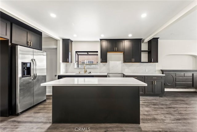 kitchen with dark wood-type flooring, stainless steel fridge with ice dispenser, sink, and a kitchen island