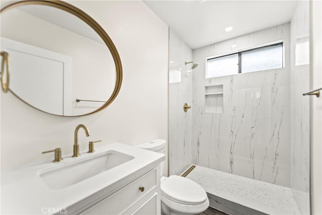 bathroom with tiled shower, vanity, and toilet