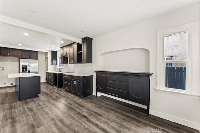 kitchen with dark hardwood / wood-style floors, a center island, decorative backsplash, sink, and stainless steel fridge with ice dispenser