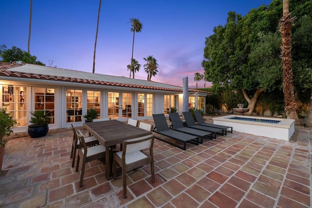 patio terrace at dusk with a swimming pool with hot tub and french doors